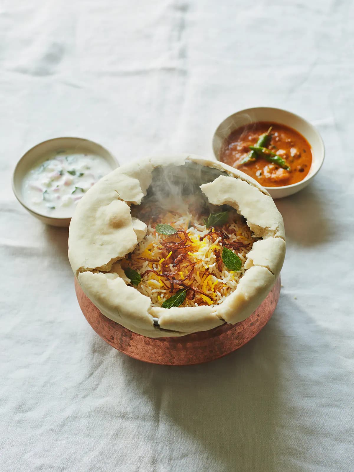 A copper handi of Hyderabadi dum biryani with raita and mirchi ka salan